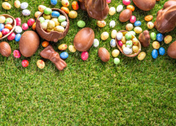 Easter egg hunting background. Various candy and chocolate Easter eggs, bunny and rabbits with basket for eggs on green grass park or garden background