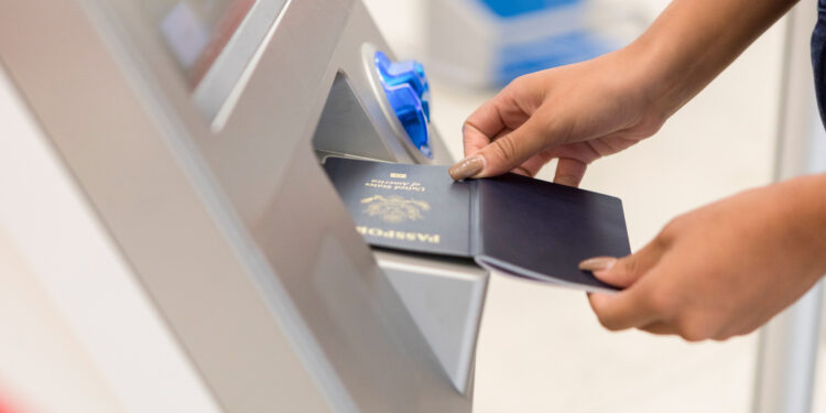 An unrecognizable woman stands in front of an airport kiosk and holds her passport open to scan it.