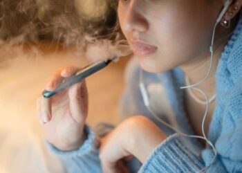 Young woman vaping an electronic cigarette for relax while working at night