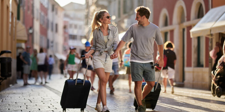 Happy couple of tourists talking while dragging their suitcases on the street.