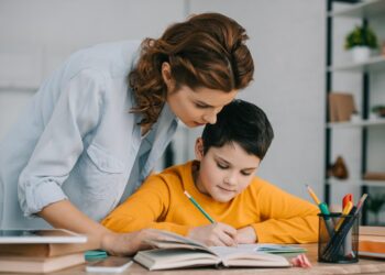 beautiful woman standing near adorable writing in copy book while doing schoolwork at home